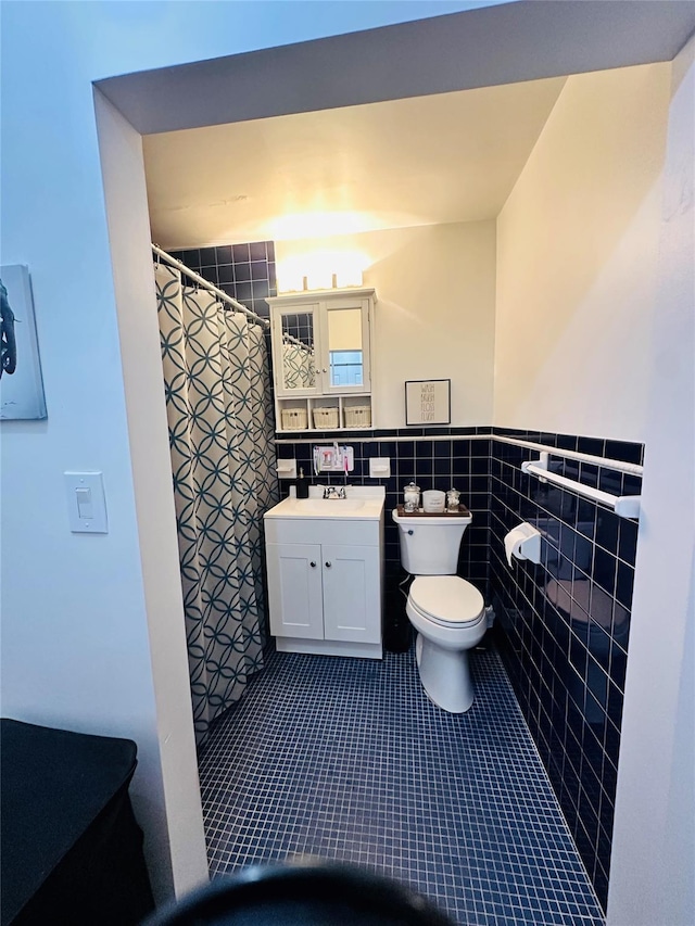 bathroom featuring toilet, a shower with shower curtain, tile patterned floors, tile walls, and wainscoting