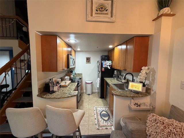 kitchen featuring a sink, stainless steel appliances, stone countertops, brown cabinetry, and baseboards