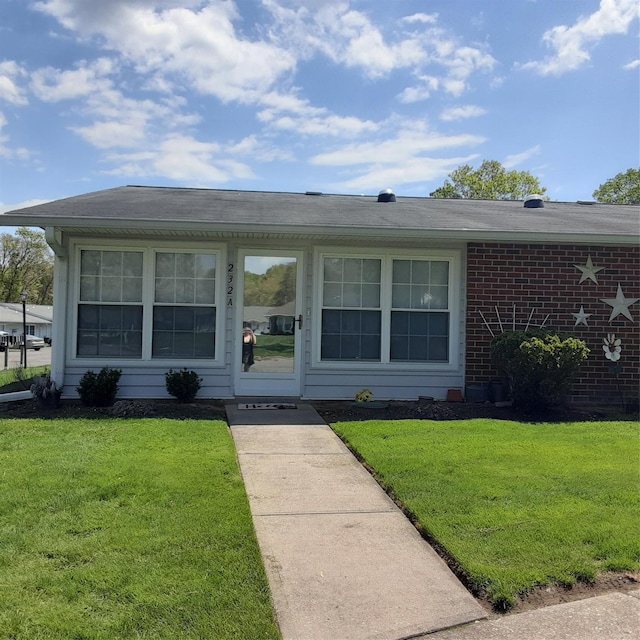 view of front of house with a front yard, brick siding, and roof with shingles