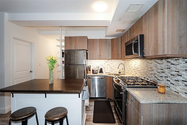kitchen with stainless steel appliances, a sink, a kitchen breakfast bar, a kitchen island, and light wood finished floors