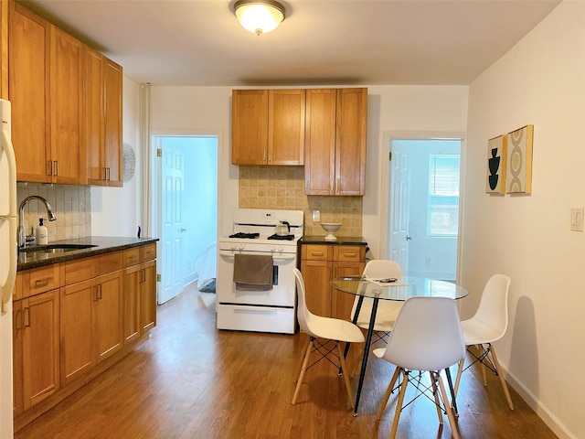 kitchen with baseboards, a sink, decorative backsplash, wood finished floors, and gas range gas stove