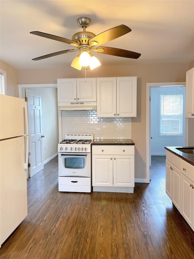 kitchen featuring under cabinet range hood, baseboards, dark wood-style flooring, white appliances, and dark countertops