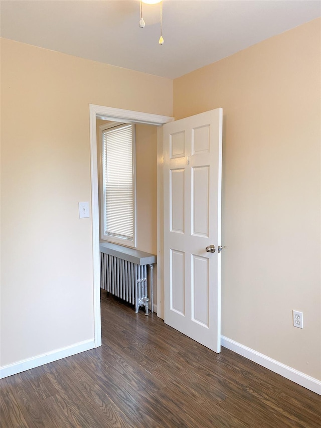 empty room with baseboards, radiator, and dark wood-style flooring