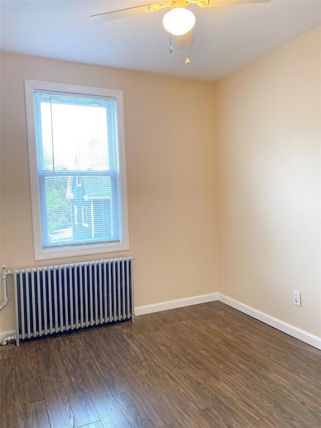 spare room with radiator, baseboards, wood finished floors, and a ceiling fan