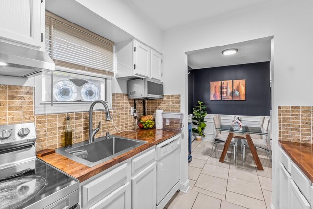 kitchen featuring appliances with stainless steel finishes, a sink, white cabinetry, light tile patterned floors, and backsplash