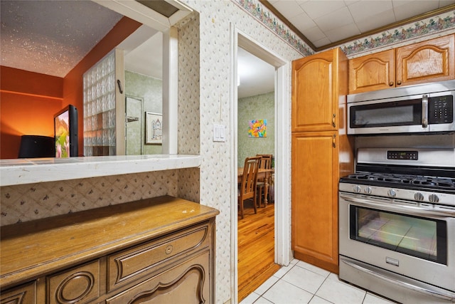 139-15 83rd Ave Unit 409, Briarwood, NY 11435 - kitchen with stainless steel appliances, wallpapered walls, light tile patterned flooring, and brown cabinets