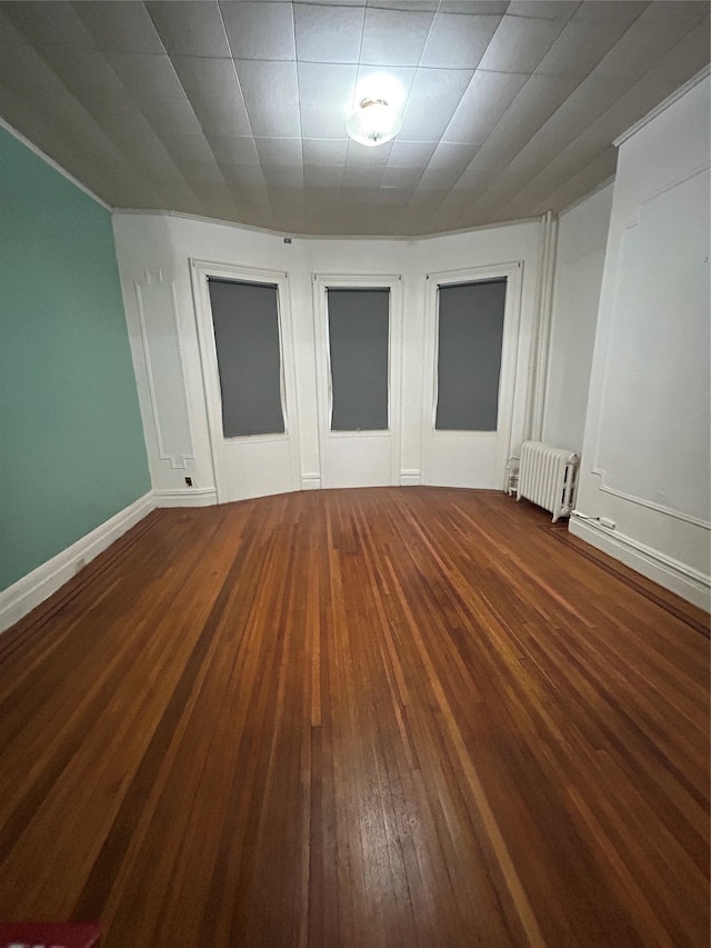 empty room featuring radiator, hardwood / wood-style floors, and baseboards