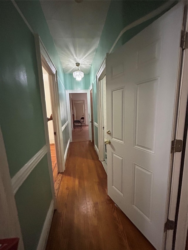 hallway with a chandelier, wood finished floors, and baseboards