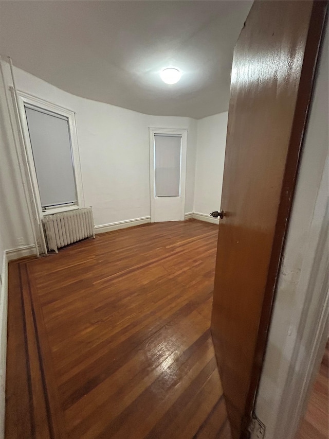 empty room with radiator, wood finished floors, and baseboards