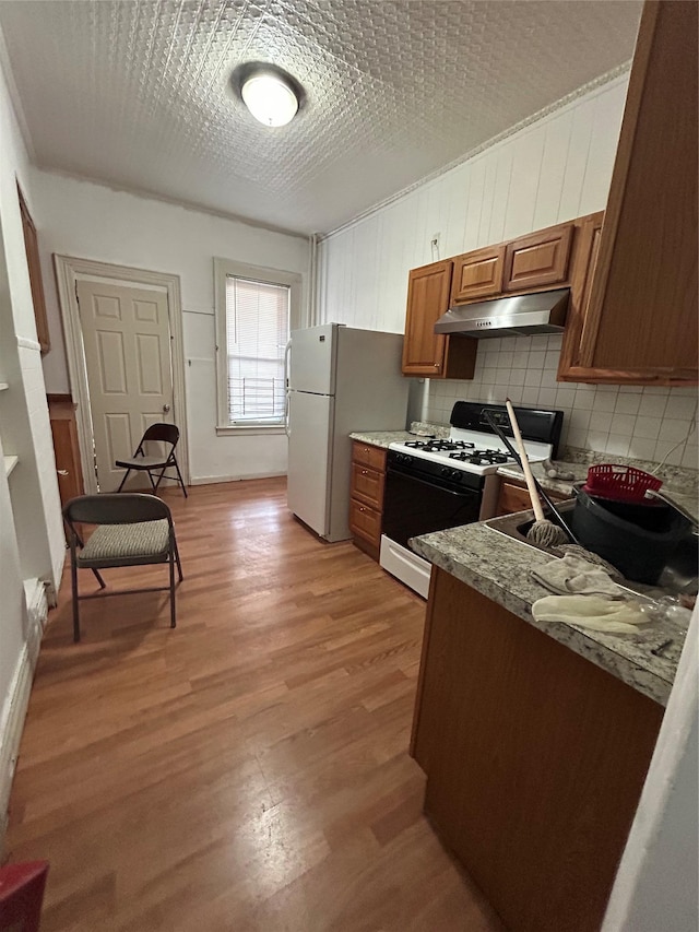 kitchen featuring range with gas cooktop, under cabinet range hood, brown cabinets, light wood-style flooring, and backsplash