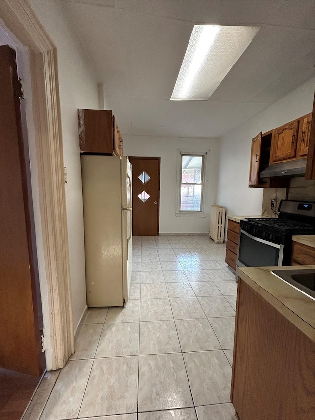 kitchen with freestanding refrigerator, gas stove, radiator, under cabinet range hood, and brown cabinetry
