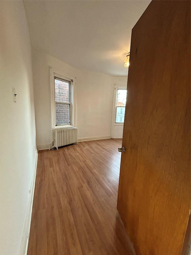 empty room with radiator, wood finished floors, and baseboards