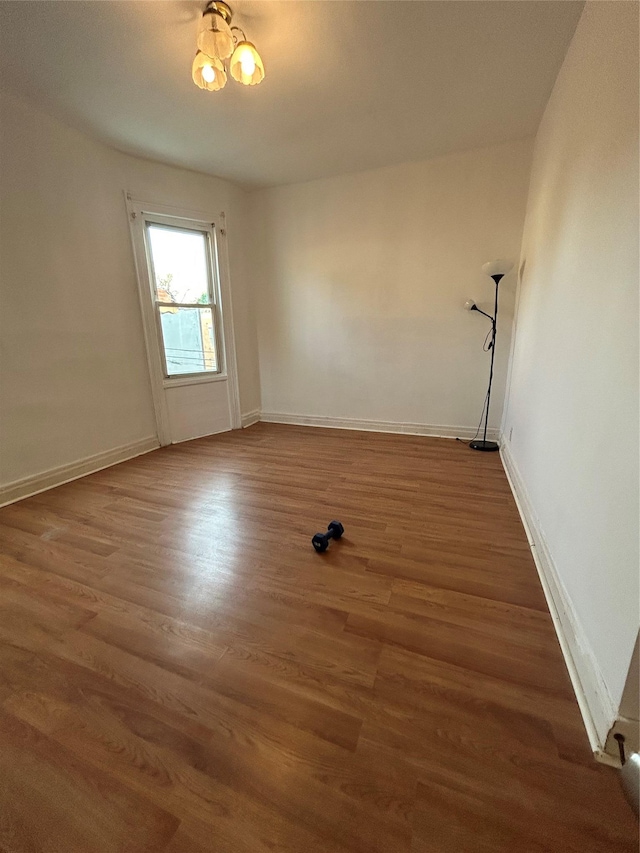 unfurnished room with a chandelier, wood finished floors, and baseboards