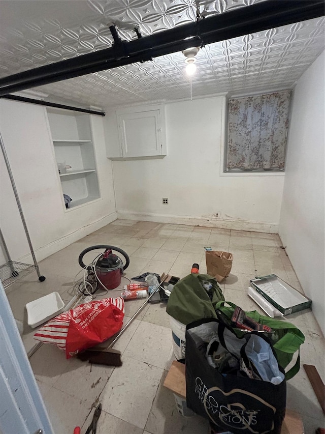 finished basement featuring built in shelves, an ornate ceiling, and baseboards