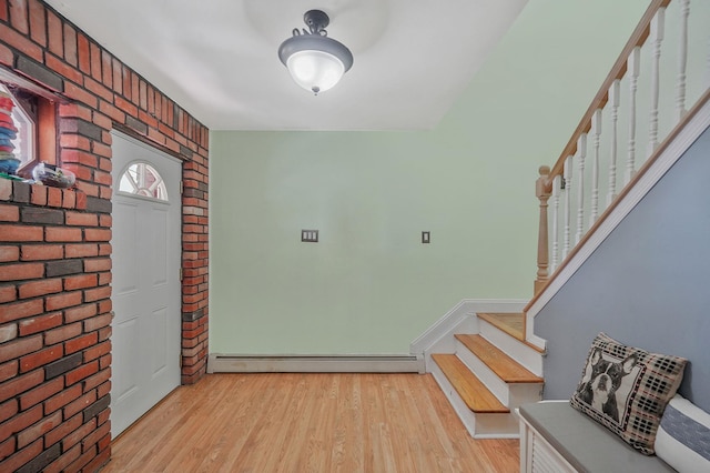 entrance foyer featuring a baseboard heating unit, stairs, brick wall, and light wood-style flooring