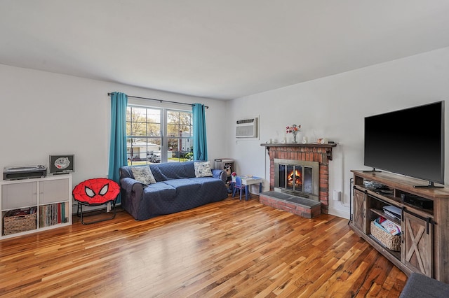 living room with wood finished floors, a brick fireplace, and a wall unit AC