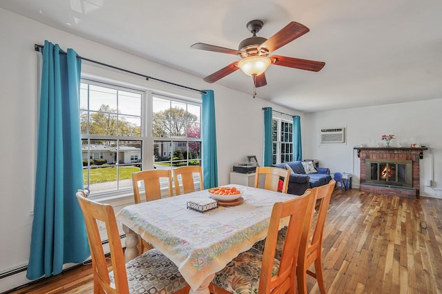 dining area with a wall unit AC, light wood-style floors, ceiling fan, a fireplace, and a baseboard heating unit