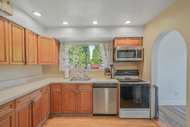 kitchen featuring appliances with stainless steel finishes, a sink, light wood-style flooring, light countertops, and arched walkways