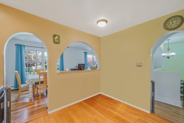 hall with light wood finished floors, baseboards, a chandelier, and arched walkways