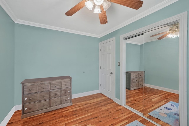 unfurnished bedroom with wood finished floors, crown molding, baseboards, a ceiling fan, and a closet