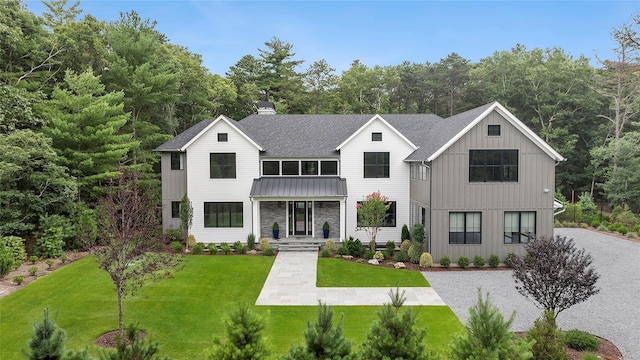 view of front of property featuring board and batten siding, roof with shingles, a chimney, a front yard, and a standing seam roof
