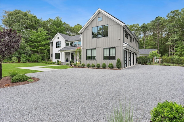 modern farmhouse style home with gravel driveway, an attached garage, board and batten siding, a standing seam roof, and a front yard