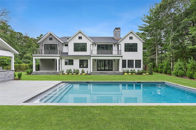 rear view of house with a balcony, an outdoor pool, a chimney, board and batten siding, and a yard
