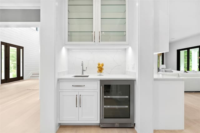 indoor wet bar with wine cooler, decorative backsplash, and light wood-type flooring