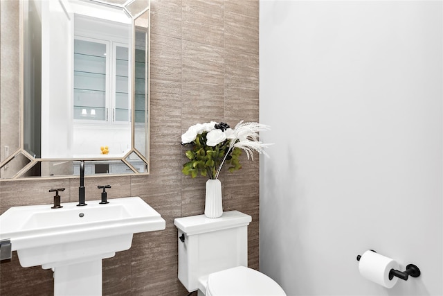 half bath with tile walls, toilet, a sink, and tasteful backsplash