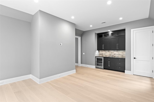 indoor wet bar with wine cooler, light wood-type flooring, decorative backsplash, recessed lighting, and baseboards