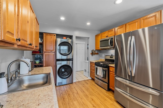 kitchen with appliances with stainless steel finishes, stacked washing machine and dryer, a sink, light countertops, and recessed lighting
