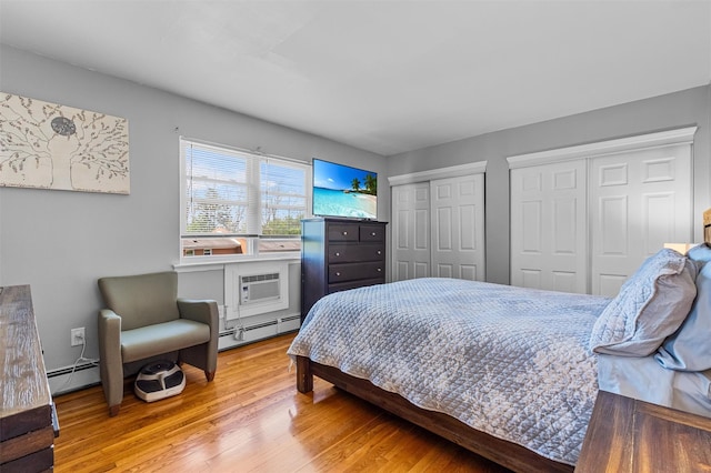 bedroom featuring baseboard heating, multiple closets, wood finished floors, and an AC wall unit