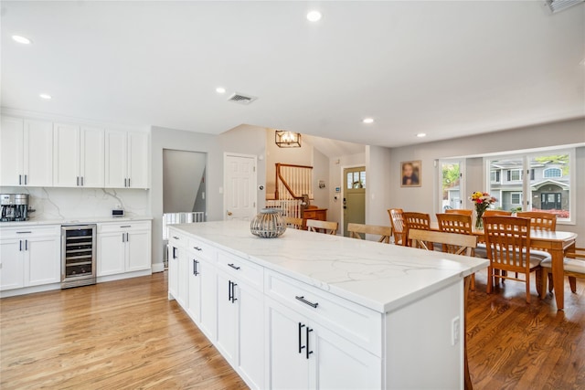 kitchen with wine cooler, light wood-style floors, recessed lighting, decorative backsplash, and a kitchen island