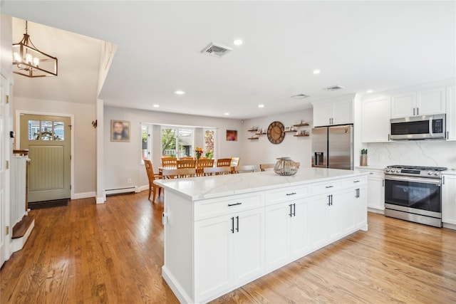 kitchen featuring appliances with stainless steel finishes, baseboard heating, a center island, light wood finished floors, and tasteful backsplash