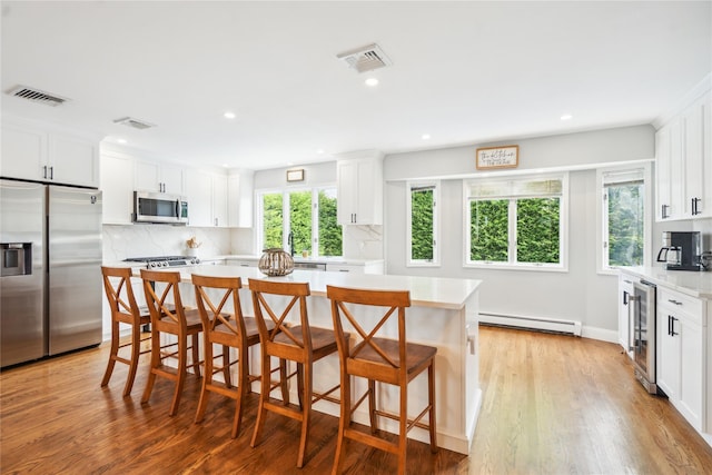 kitchen featuring stainless steel appliances, a baseboard radiator, wine cooler, light countertops, and white cabinets