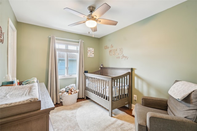 bedroom featuring wood finished floors, a crib, ceiling fan, and baseboards