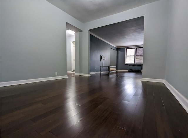 unfurnished living room with radiator, dark wood-style flooring, and baseboards