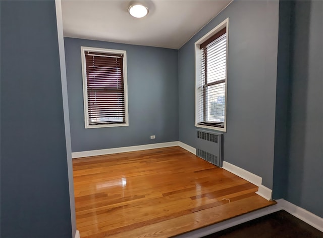 empty room with radiator heating unit, wood finished floors, and baseboards