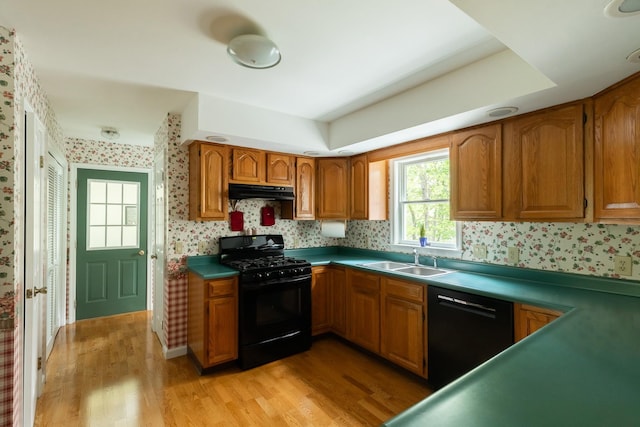 kitchen featuring black appliances, wallpapered walls, a sink, under cabinet range hood, and light wood-style floors