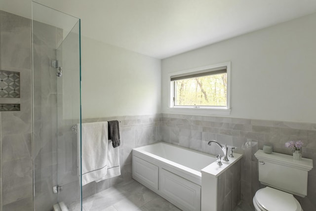 full bath with tile walls, a shower stall, a bath, toilet, and a wainscoted wall