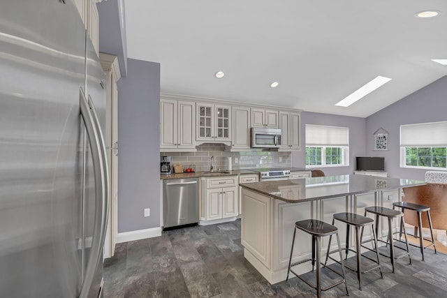 kitchen with appliances with stainless steel finishes, a skylight, a breakfast bar area, lofted ceiling, and a sink
