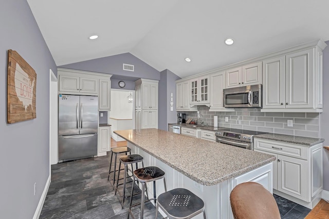 kitchen with stainless steel appliances, vaulted ceiling, baseboards, backsplash, and a breakfast bar