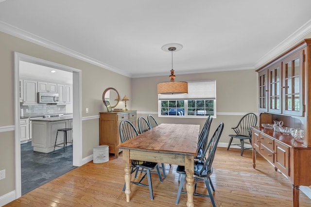 dining space featuring light wood finished floors, crown molding, and baseboards
