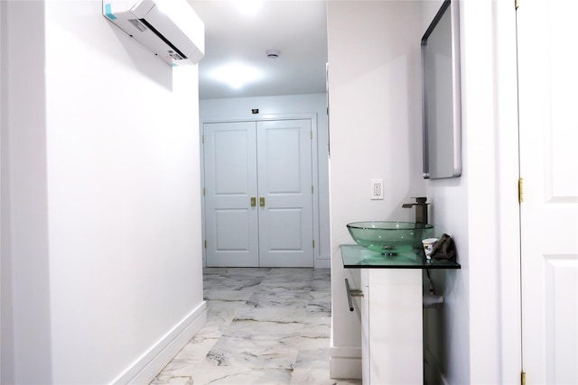 hallway featuring marble look tile flooring, a sink, baseboards, and a wall unit AC