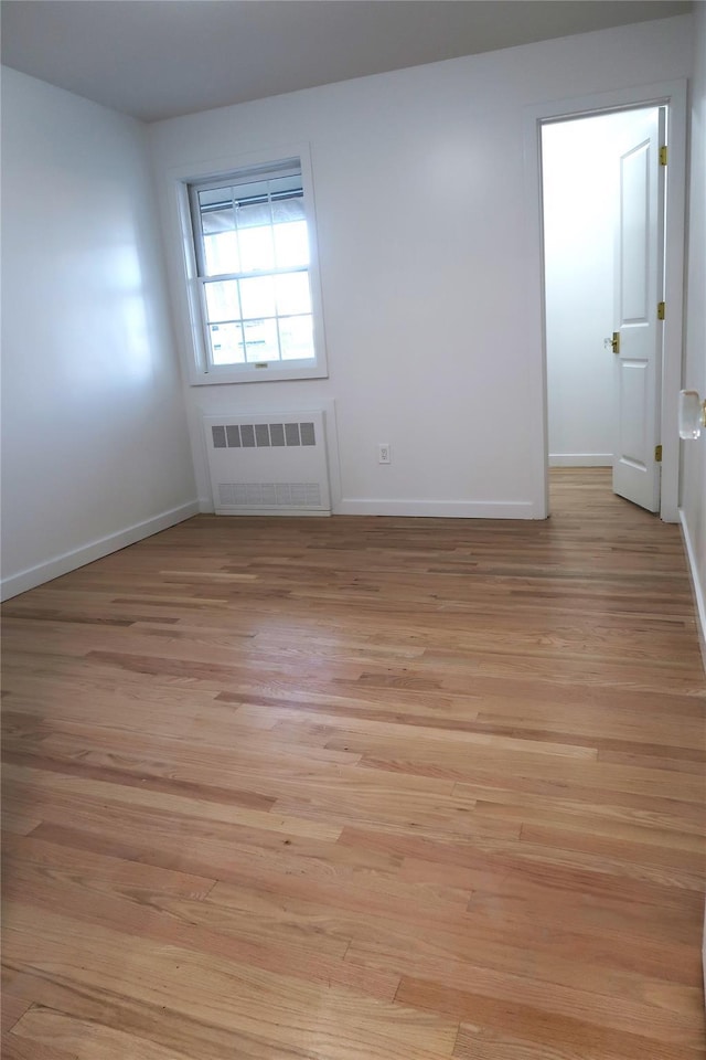 spare room with radiator, light wood-style floors, and baseboards
