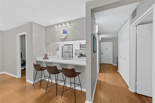 25 Rockledge Ave Unit 501, White Plains, NY 10601 - kitchen with appliances with stainless steel finishes, a breakfast bar, white cabinets, a textured ceiling, and light wood finished floors