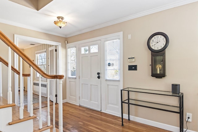 foyer with radiator heating unit, wood finished floors, stairs, crown molding, and baseboards