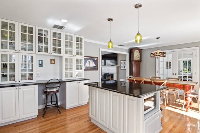 kitchen with stainless steel microwave, white cabinets, glass insert cabinets, light wood-type flooring, and crown molding