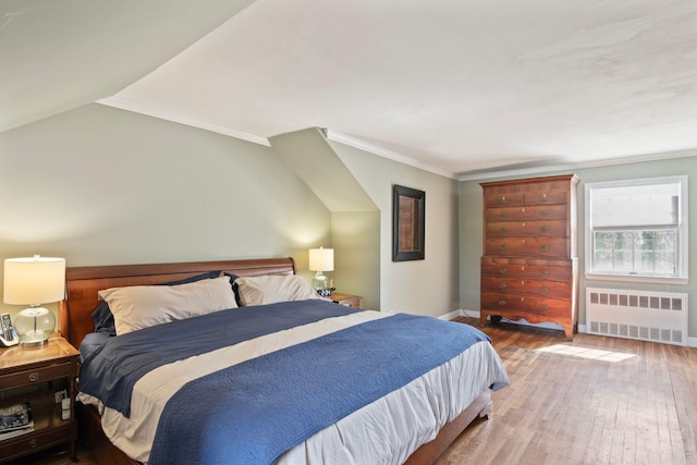 bedroom featuring radiator, wood-type flooring, baseboards, lofted ceiling, and crown molding