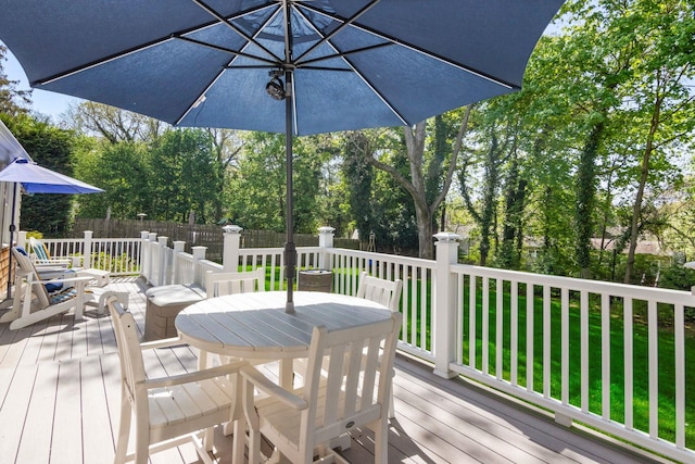 wooden terrace featuring outdoor dining space, fence, and view of scattered trees